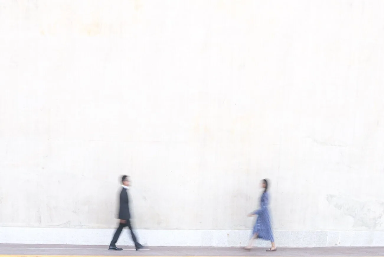 A couple walking past a pale stone wall, blurred with movement