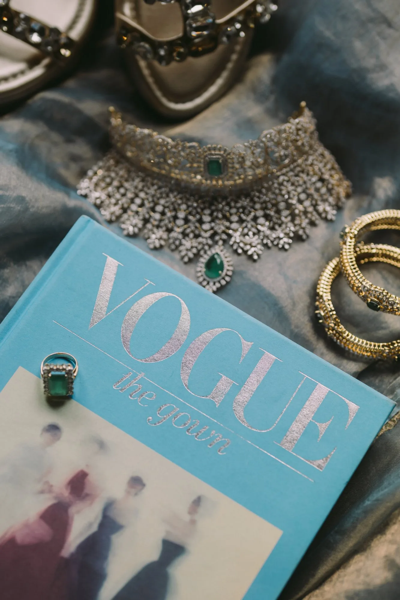 An emerald and diamond choker, gold bangles, an emerald ring and jewelled shoes laid out on grey silk