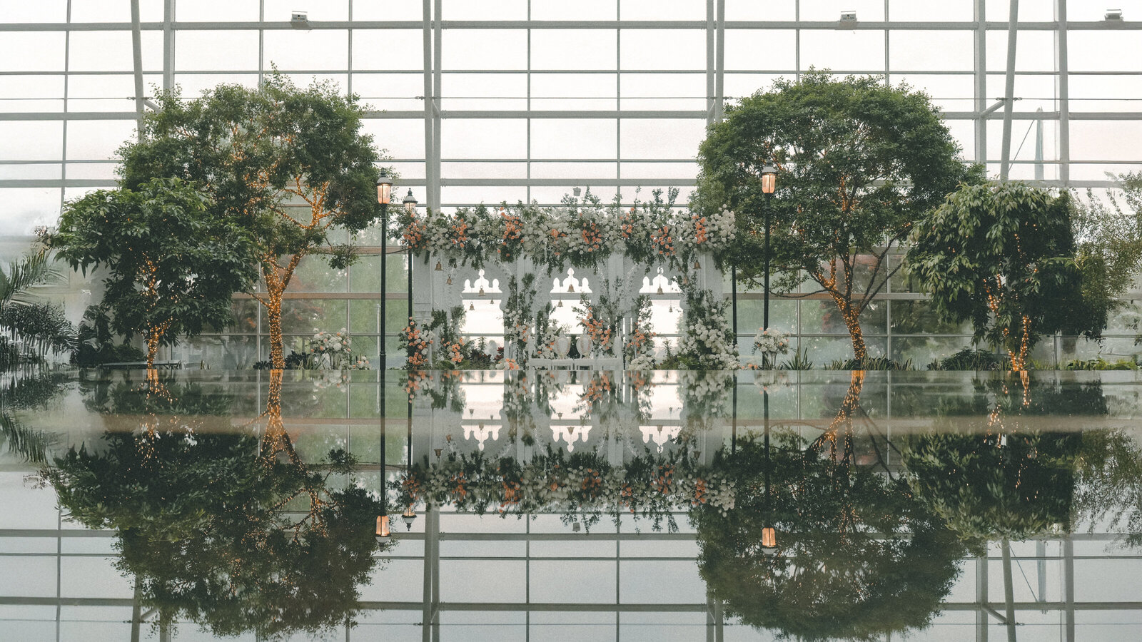 A mandap reflected in still water beneath a glass atrium at the Gaylord National Resort
