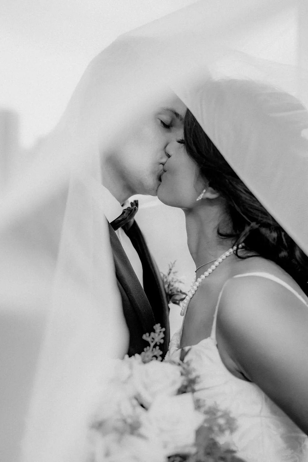A black-and-white frame of a couple kissing beneath a veil