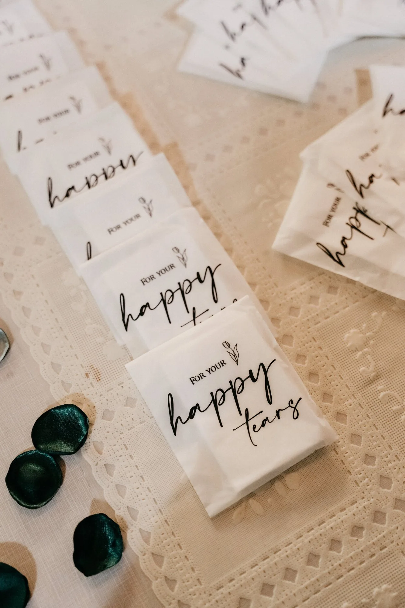 Tissue packets printed “for your happy tears” laid along a lace table runner with green petals