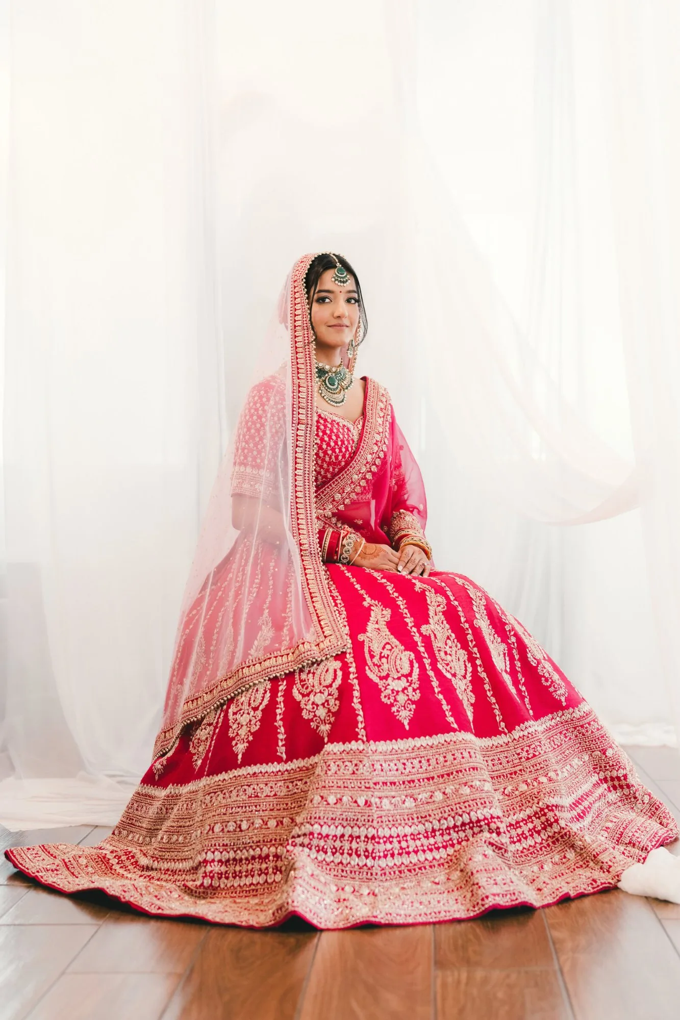 A bride in red with her chooda, photographed beneath her veil before the ceremony
