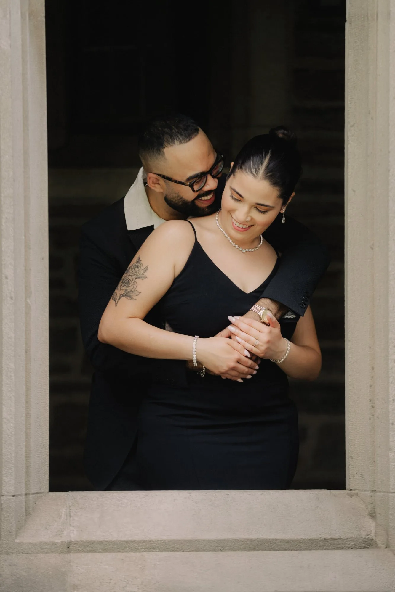 An engaged couple framed in a carved stone window, laughing together